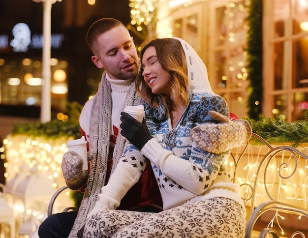 Joven pareja feliz disfrutando de su cita romántica mientras se calienta con bebidas calientes.