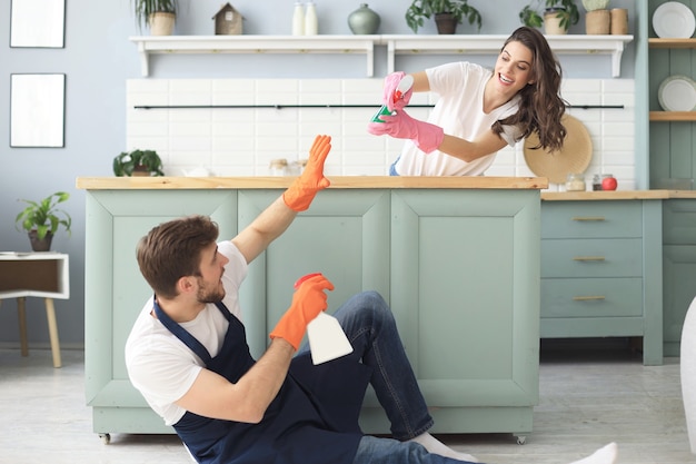 Joven pareja feliz se divierte mientras hace la limpieza en casa.