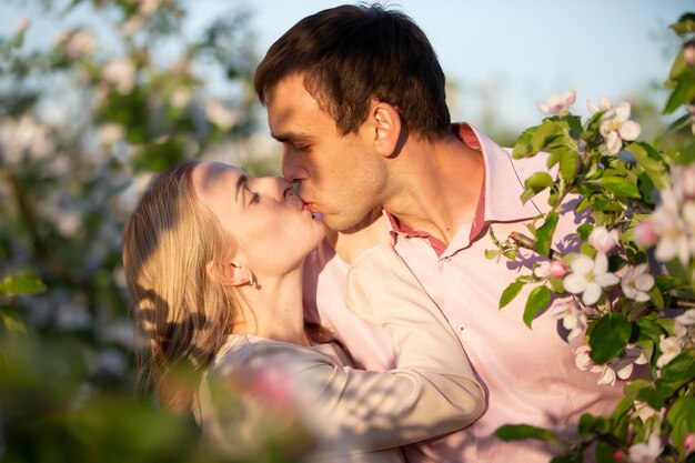 Joven pareja feliz enamorada al aire libre amando al hombre y a la mujer en un paseo por un parque floreciente de primavera