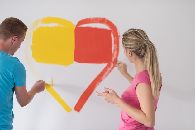 Una joven pareja feliz está pintando un corazón en la pared mientras repara en casa.