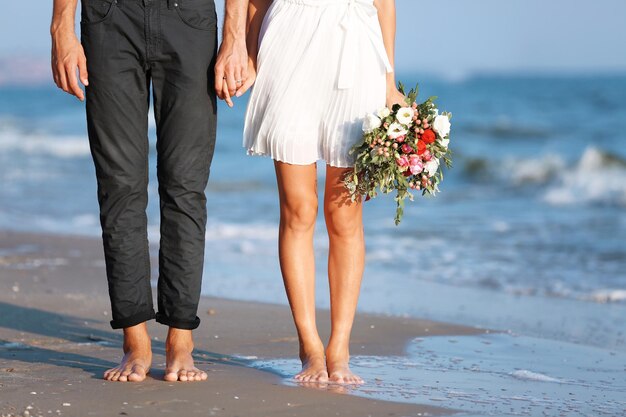 Joven pareja feliz con flores caminando por la orilla del mar