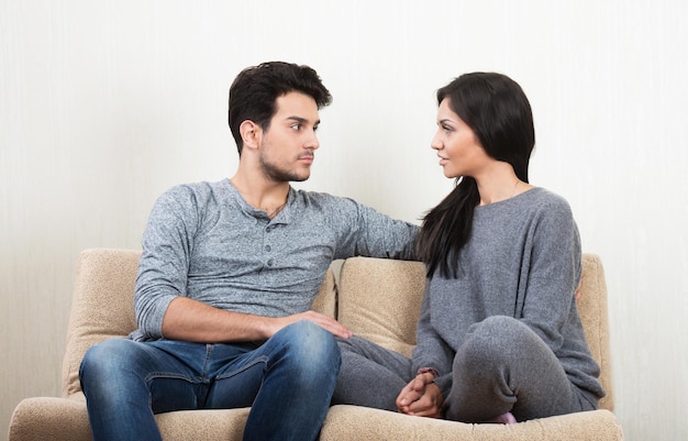 Una joven pareja feliz hablándose sentada en un sofá