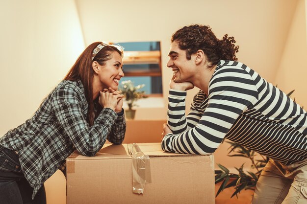 La joven pareja feliz se muda a una nueva casa. Están empacando cajas con cosas para su nueva sala de estar.