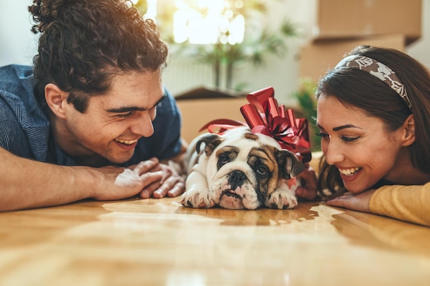 La joven pareja feliz se muda a una nueva casa. Están tumbados en el suelo con su cachorrito después de llevar cajas con cosas a su nuevo hogar.