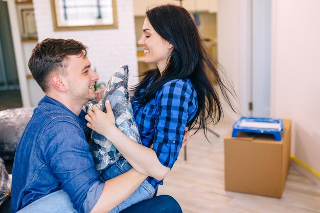 Foto una joven pareja feliz se muda a un nuevo apartamento y se ríe, salta, juega con almohadas