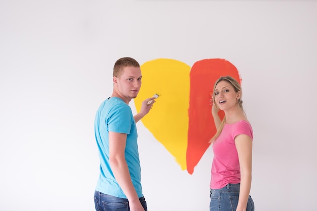 Foto una joven pareja feliz está pintando un corazón en la pared mientras repara en casa.