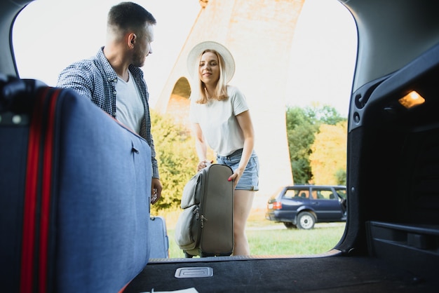 Foto joven pareja feliz preparándose para ir de vacaciones. poner las maletas en el maletero del coche