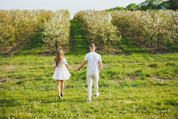 Una joven pareja feliz en previsión del embarazo camina por un jardín floreciente Pareja enamorada en manzanos florecientes