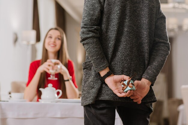 Una joven pareja feliz en el restaurante y un joven esconden una pequeña caja con regalo