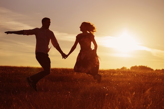 Joven pareja feliz saltando al atardecer