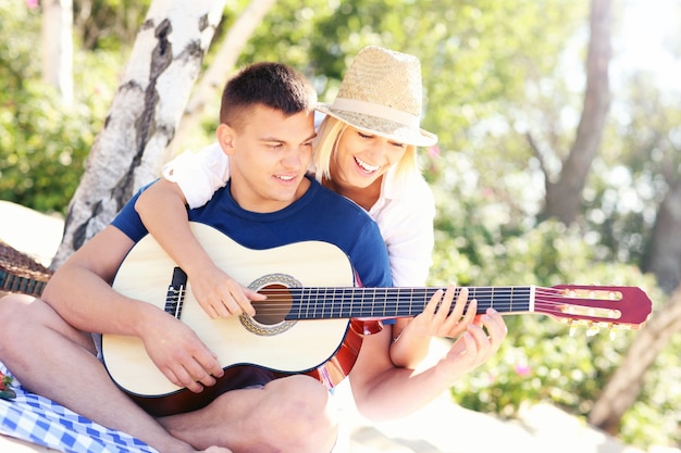 joven pareja feliz sentados juntos en la playa y tocando la guitarra