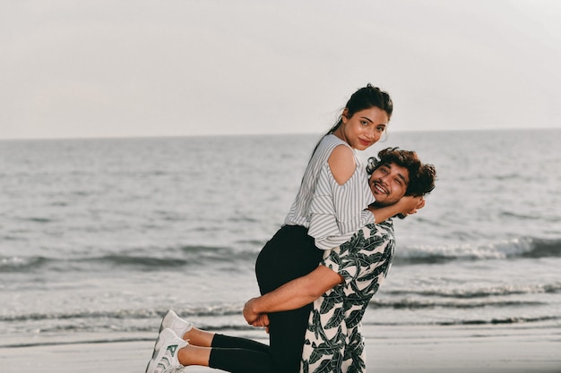 joven pareja feliz sosteniendo en brazos en la playa modelo pakistaní indio