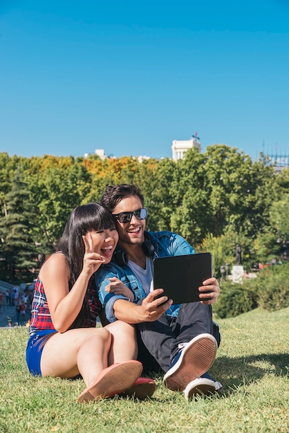 Foto joven pareja feliz con tableta sentado en el parque