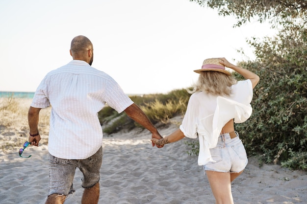 Joven pareja feliz tomados de la mano y caminando juntos a la playa en verano