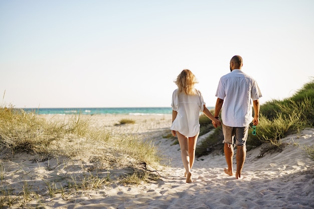 Joven pareja feliz tomados de la mano y caminando juntos a la playa en verano