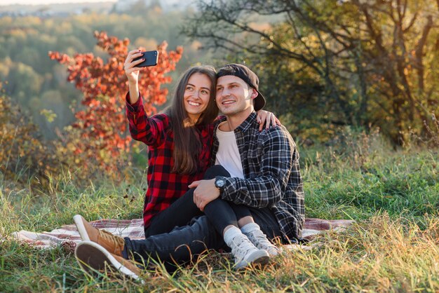 Joven pareja feliz tomando selfie con smartphone en el parque.