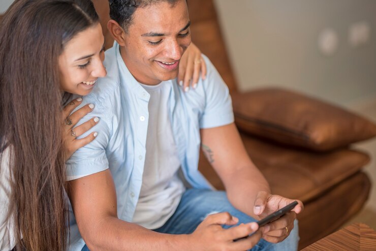 Foto joven pareja feliz usa teléfonos inteligentes juntos en casa sentados en el sofá - gente interracial alegre de niña y niño que usa celular para enviar mensajes y divertirse - concepto de relación de amor y vida