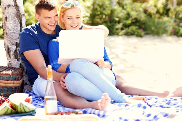 una joven pareja feliz usando la computadora portátil en la playa