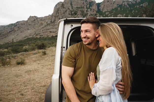 Joven pareja feliz en un viaje por carretera sentado en el maletero del coche