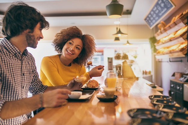 Foto joven pareja fresca desayunando, están tomando té y café en una panadería, naranja