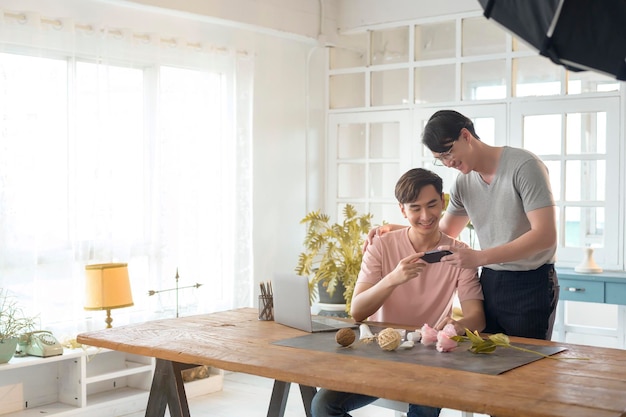 Joven pareja gay sonriente trabajando en un nuevo proyecto y tomando fotos de un nuevo producto por teléfono inteligente