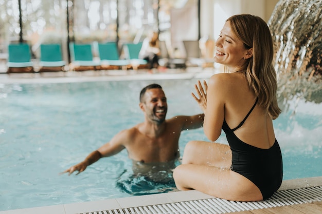 Joven pareja guapa divirtiéndose en la piscina cubierta