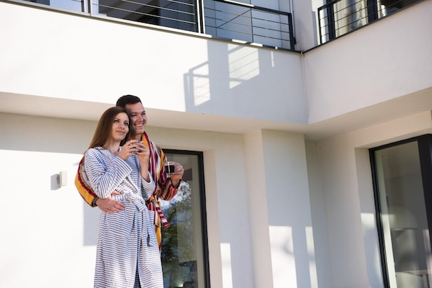 Joven pareja hermosa en batas de baño está disfrutando del café de la mañana frente a su villa de lujo