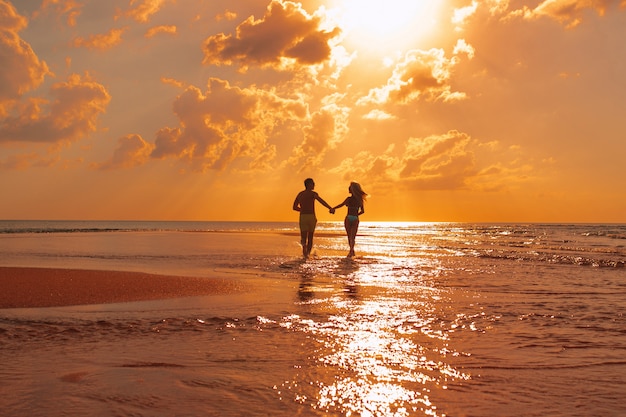 Joven pareja hermosa camina por la orilla del mar al atardecer. Luna de miel. Viaje romántico