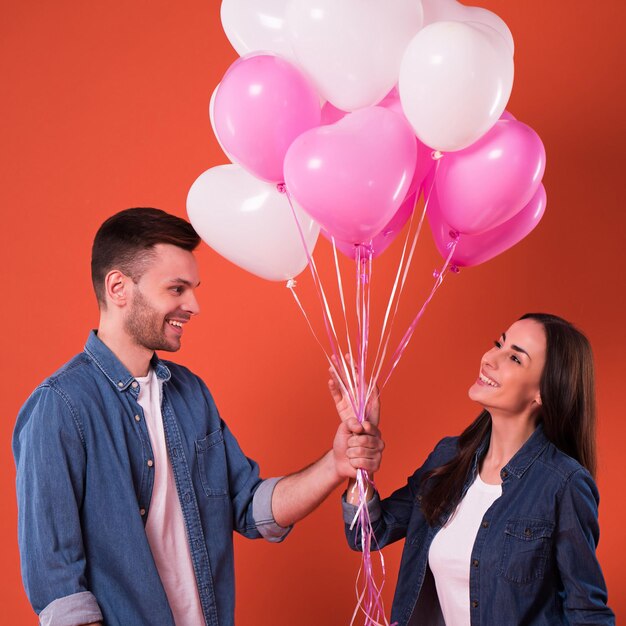 Joven pareja hermosa enamorada está posando junto con globos coloridos en ropa informal mientras celebra el día de San Valentín.