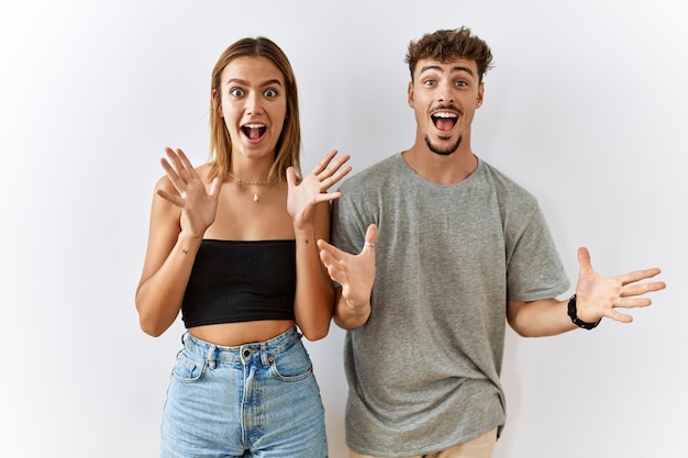 Joven pareja hermosa de pie juntos sobre un fondo aislado celebrando loco y asombrado por el éxito con los brazos levantados y los ojos abiertos gritando emocionado concepto de ganador