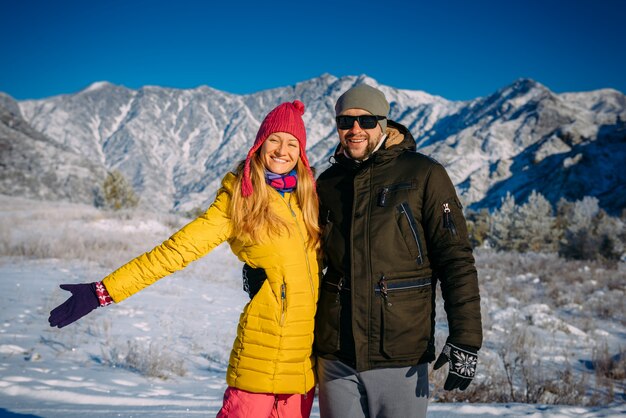 Joven pareja hermosa en ropa brillante en el fondo de montañas nevadas