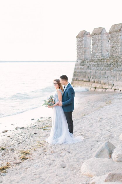 Joven pareja hermosa en ropa elegante azul abrazando cerca del castillo del lago en Sirmione. Lago de Garda, Italia