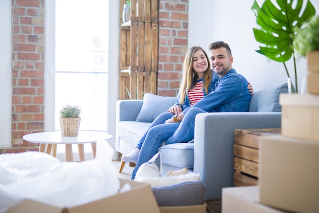 Foto joven pareja hermosa sentada y abrazándose en el sofá en un apartamento nuevo con cajas de cartón a su alrededor muy emocionada por mudarse a un nuevo hogar