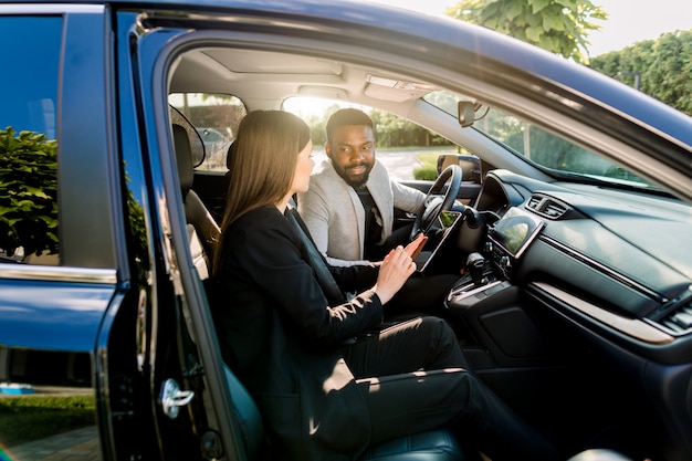 Joven pareja hermosa, socios comerciales, hombre y mujer multiétnicos, usando tableta en el viaje de negocios de automóviles