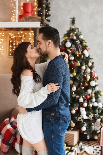 Joven pareja heterosexual dulce posando en el interior de la sala de estar decorada para las vacaciones de año nuevo