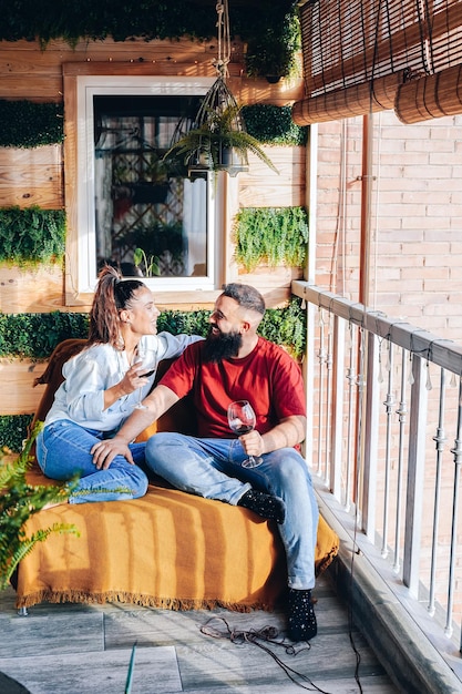 Una joven pareja heterosexual sonriente sentada una al lado de la otra y bebiendo una copa de vino