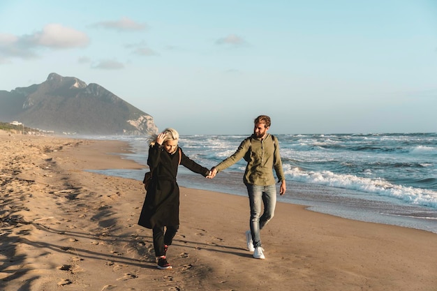 Joven pareja hipster enamorada caminando juntos al atardecer a lo largo de la playa desierta durante la temporada de otoño Concepto de amor y juventud