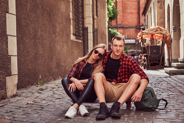Joven pareja hipster feliz, descansa durante un paseo sentado en la acera en una vieja calle de Europa.