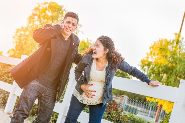 Una joven pareja hispana embarazada aturdida y con dolor caminando al aire libre