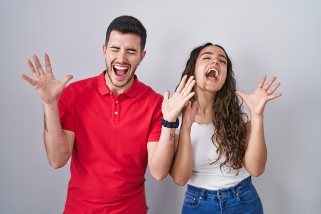 Foto joven pareja hispana de pie sobre un fondo aislado celebrando loco y loco por el éxito con los brazos levantados y los ojos cerrados gritando emocionados. concepto de ganador