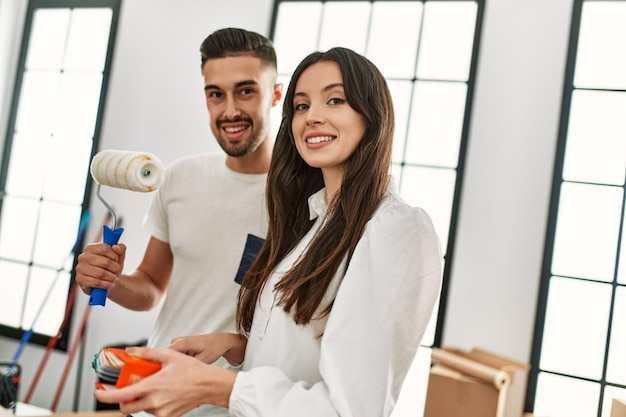 Joven pareja hispana pintando con rodillo de pintura en un nuevo hogar