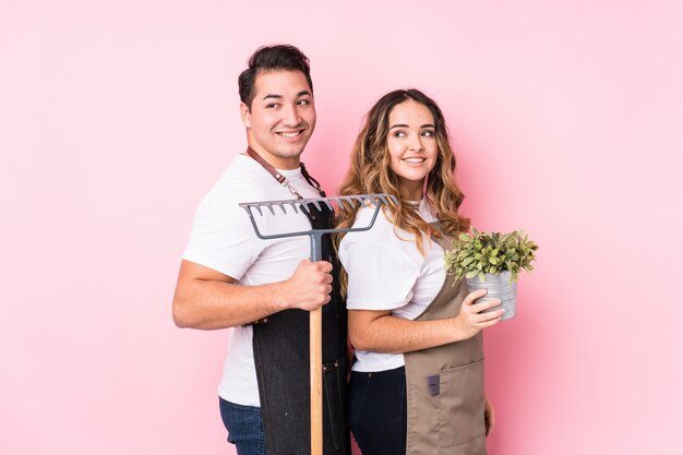 Joven pareja jardinero aislado mira a un lado sonriente, alegre y agradable.