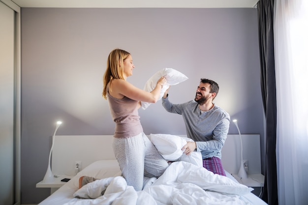 Foto joven pareja juguetona teniendo pelea de almohadas en la mañana en el dormitorio
