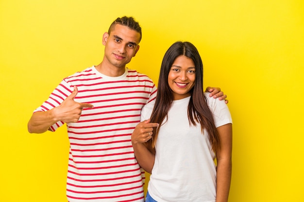 Joven pareja latina aislada sobre fondo amarillo persona apuntando con la mano a un espacio de copia de camisa, orgulloso y seguro