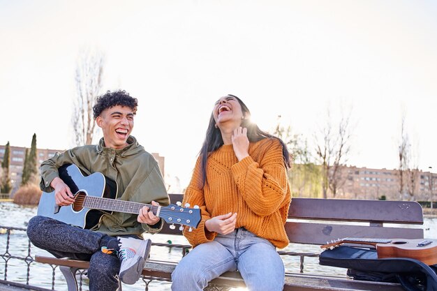 Joven pareja latina sentada en un banco El hombre le toca una canción a la mujer, se ríen y se divierten