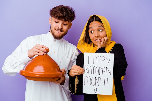 Joven pareja marroquí vistiendo un traje típico árabe celebrando el Ramadán aislado sobre fondo púrpura