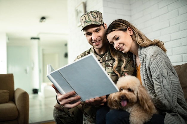 Joven pareja militar feliz mirando un álbum de fotos mientras se reúne en casa