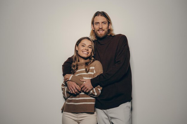 Foto una joven pareja de moda abrazada y mirando a la cámara con sonrisas en un fondo beige