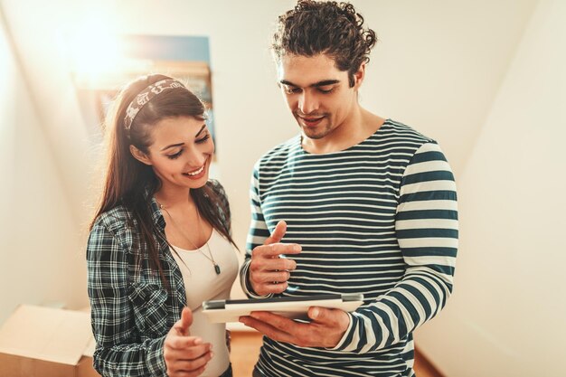 La joven pareja se muda a una nueva casa. Están mirando una tableta digital y discutiendo ideas de renovación.