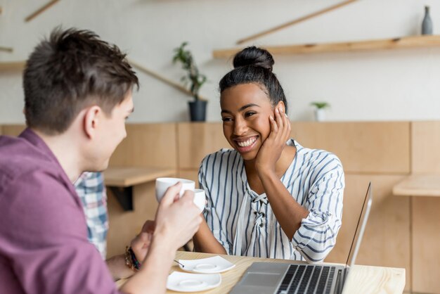 una joven pareja multiétnica feliz bebiendo café y sonriéndose entre sí en una cafetería